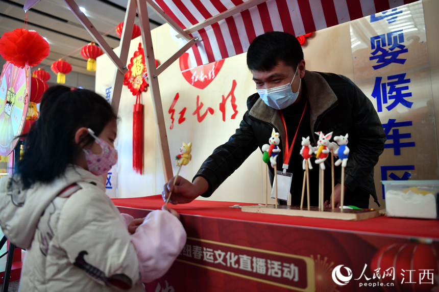 春運首日，車站設置非遺展示區(qū)，傳承人將捏好的泥人遞給一名小旅客。人民網(wǎng) 時雨攝